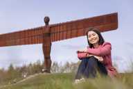 Woman sitting on grass bank with the Angel of the North visible in the background.