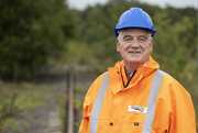 A man in a hard hat and hi-vis jacket, standing next to a train track.